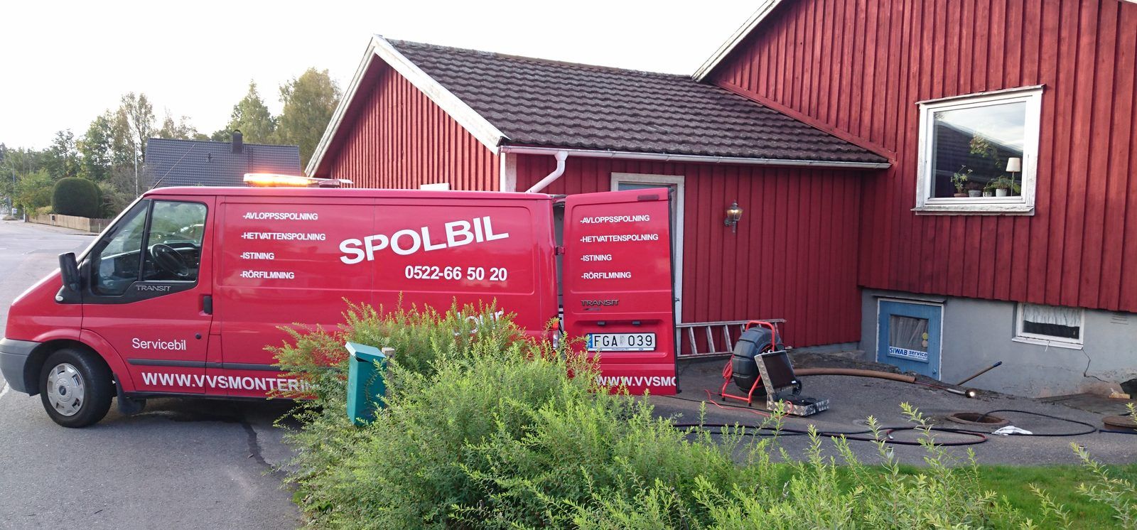 VVS Monterings röda spolbil står med öppna bakdörrar framför ett rött trähus, med spolutrustning framme på uppfarten.